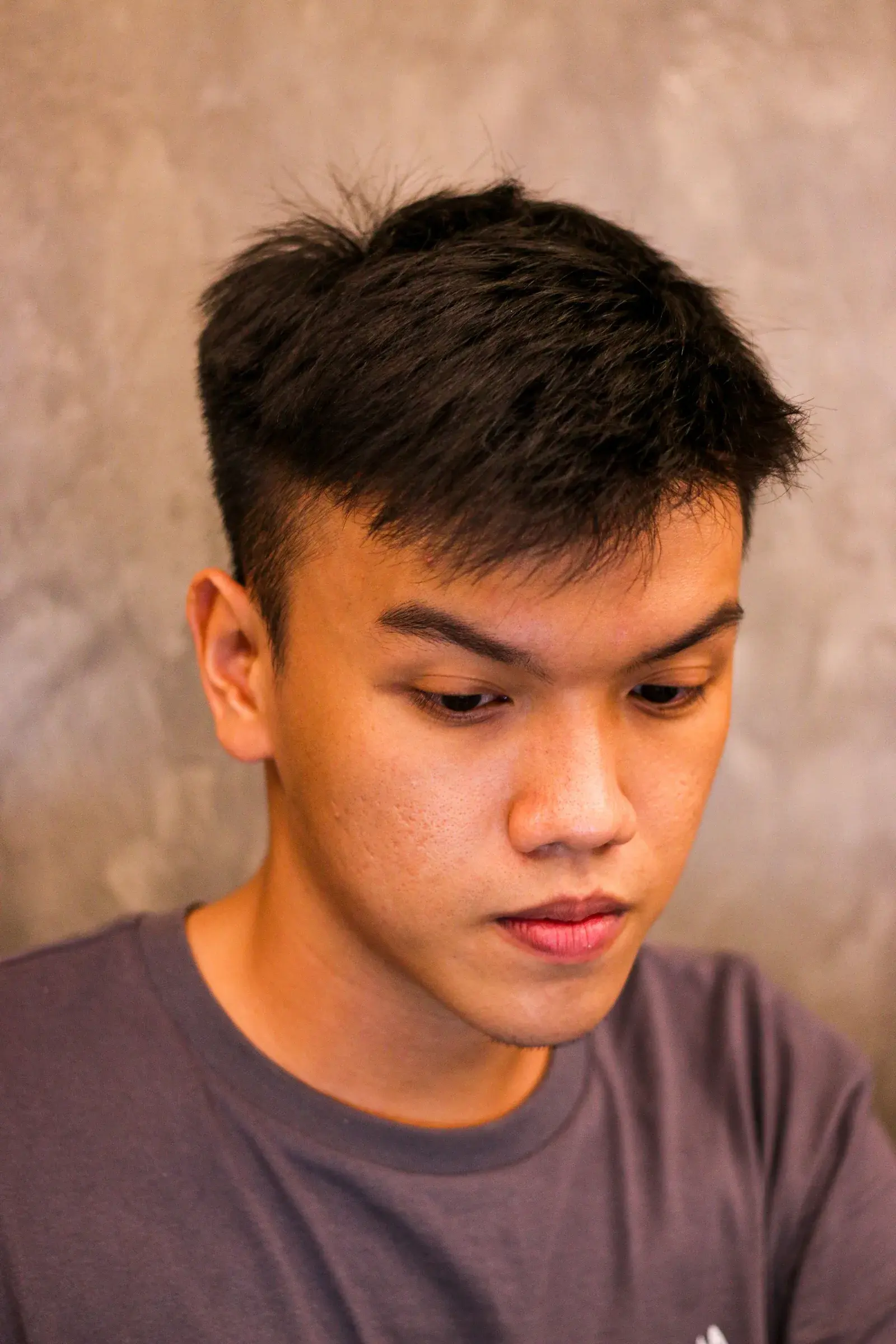Man with short textured dark hair and a tapered haircut in three-quarter view